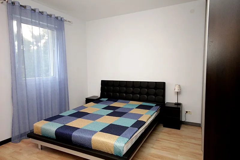 Bedroom featuring a checkered bed, black headboard, nightstands, and blue sheer curtains over a window.