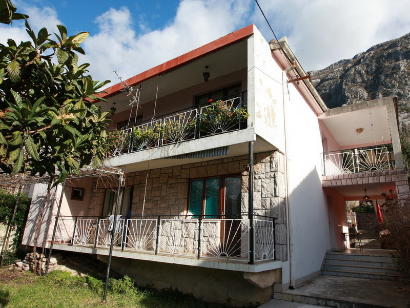 Two-story house in Dobrota, Montenegro: stone facade finish, spacious balconies with wrought-iron railings, and mountain views.