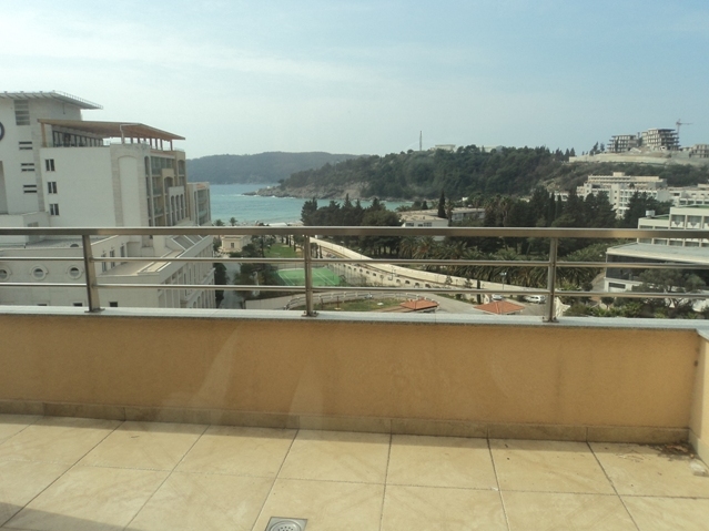 View from the apartment balcony in Bečići, Montenegro: a panorama of the sea, mountains, and resort infrastructure with a tennis court.