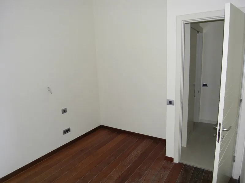 Empty room with wooden floor and white walls, an open door leads to a hallway.