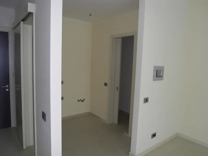 Empty room with white walls, doorways, and unfinished outlets. A water pipe protrudes from the wall.