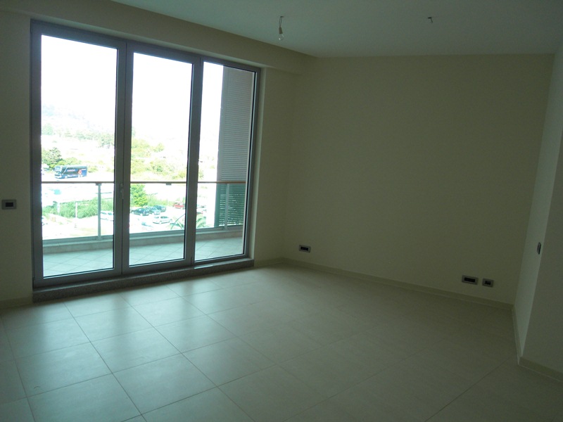 Bright living room in a new apartment in Budva, Montenegro, with panoramic windows, access to the balcony, and tiled flooring.