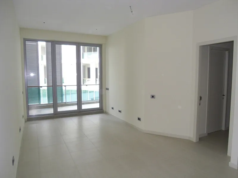 Empty room with light walls, tiled floor, and large glass doors leading to a balcony.
