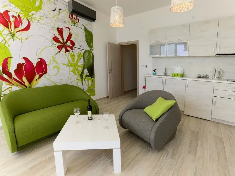 Living room with a green sofa, white coffee table, and visible kitchen area against floral wallpaper.