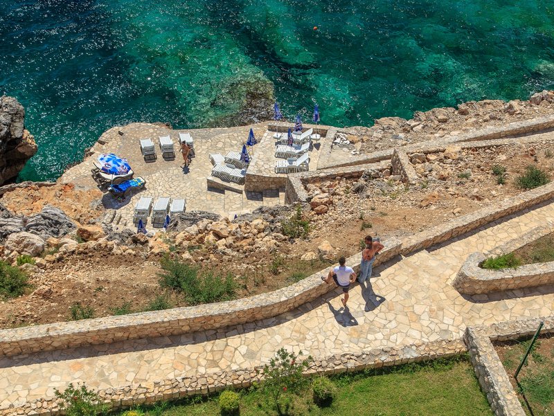 Private beach with sun loungers by the sea in Dobra Voda, Montenegro: top view of a stone terrace and azure water.