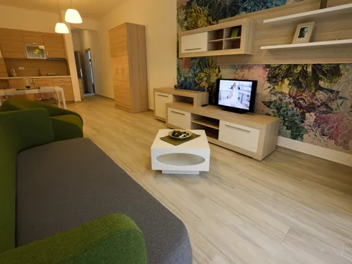 Living room with green sofa, white table, and TV against a floral mural wall.