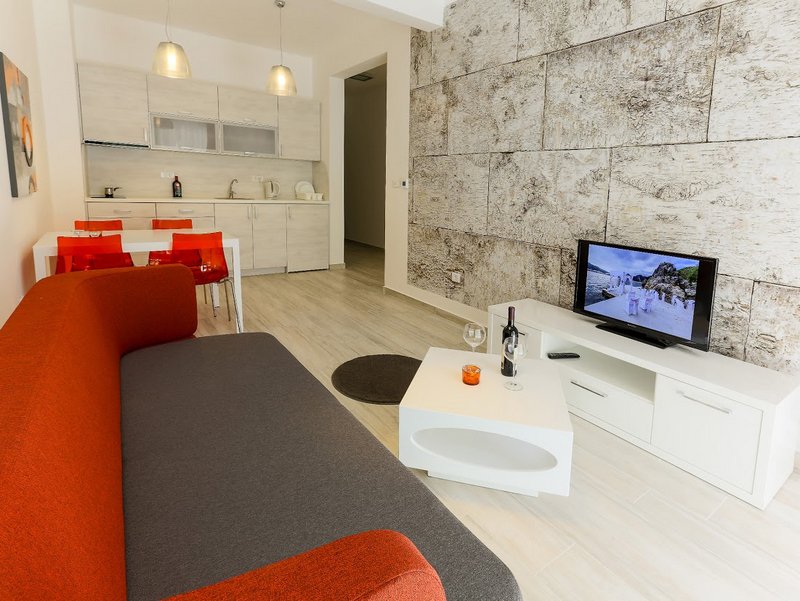 Living room with kitchen in an apartment in Dobri Vody, Montenegro: modern furniture, stone wall, and dining area.