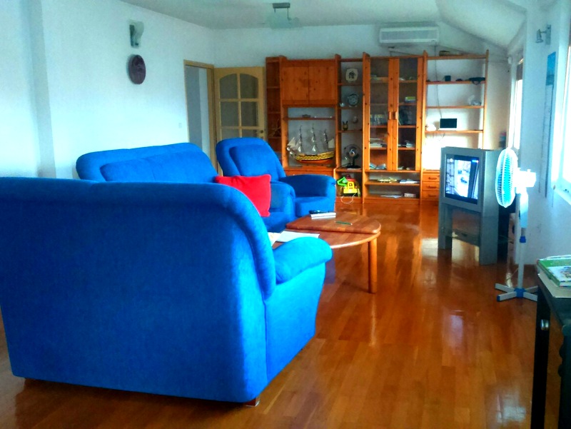 Living room in an apartment in Budva, Montenegro: blue sofas, wooden floor, shelving unit, and a TV in the interior.