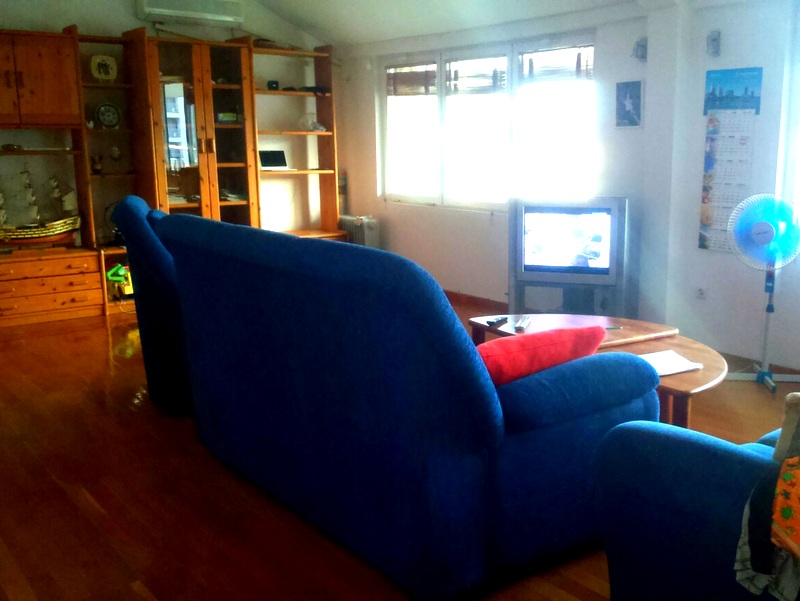 Living room in an apartment in Budva, Montenegro: blue sofa, wooden furniture, parquet floor, and a TV by the window.