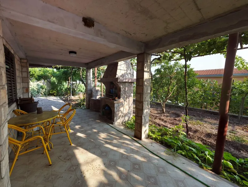 Covered terrace with yellow furniture and stone grill, garden view visible.
