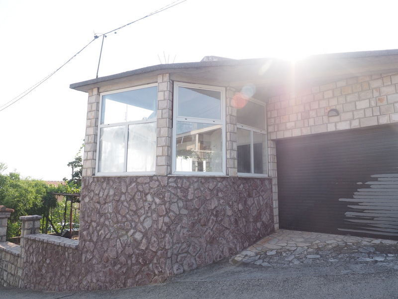 House facade in Shushan, Montenegro: stone wall cladding, panoramic windows, and a garage with roller doors.