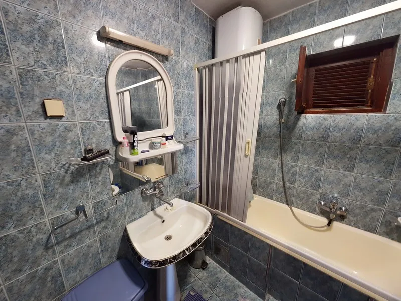 Bathroom with blue tiles, sink, mirror, and bathtub featuring a folding shower screen.