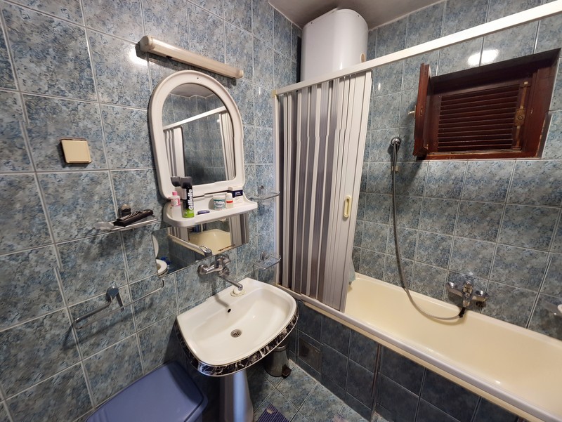 Bathroom in a house, Shushan, Montenegro: blue-toned tiles, sink, bathtub with shower curtain, and water heater.