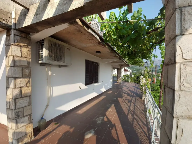 Long open balcony with brown tiles, stone columns, and a wall-mounted air conditioner unit.