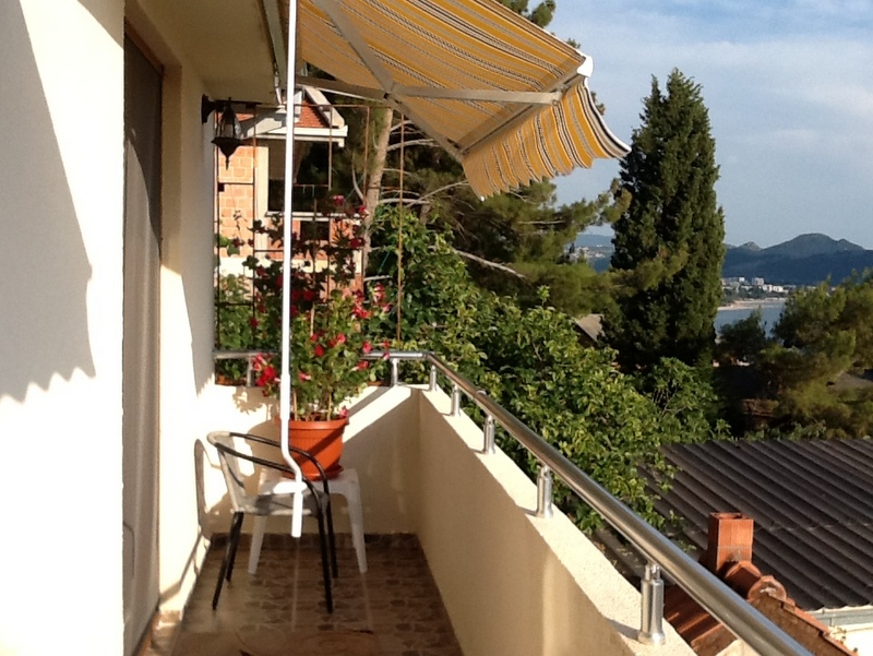 Balcony with an awning and sea view in a house in Shushan, Montenegro: chairs, potted flowers, and a panoramic landscape.