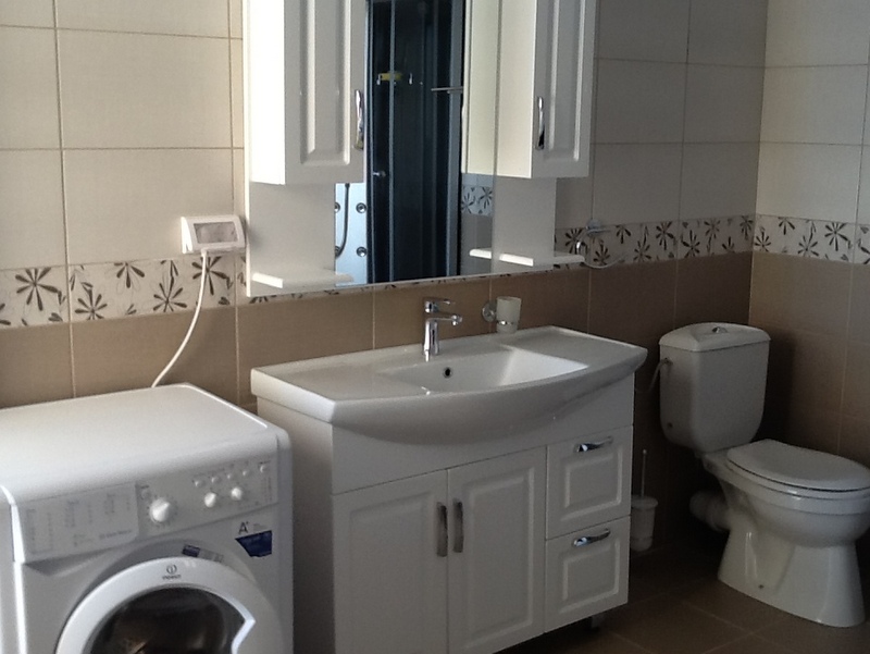 Bathroom in a house, Shushan, Montenegro: light tiles, vanity with sink, mirror, and washing machine.