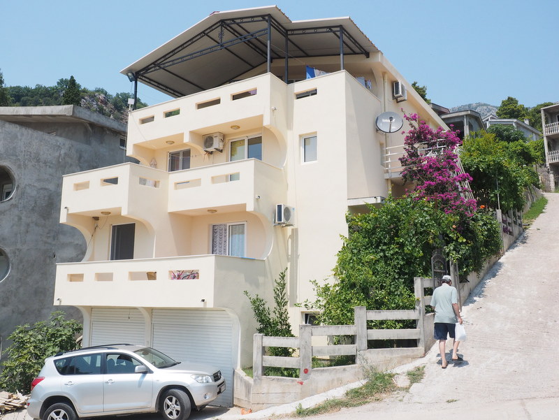 Three-story house in Bar, Montenegro: light-colored facade, terraces, garage, and blooming bougainvillea on the grounds.