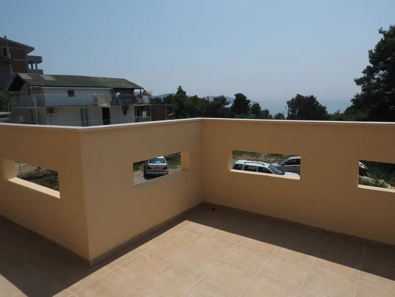 Open terrace with a beige wall featuring rectangular cutouts, overlooking parked cars and the sea.