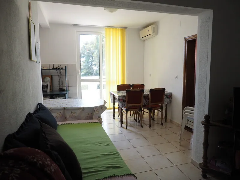 Living room featuring a sofa, dining table with chairs, and a kitchen area in the background.