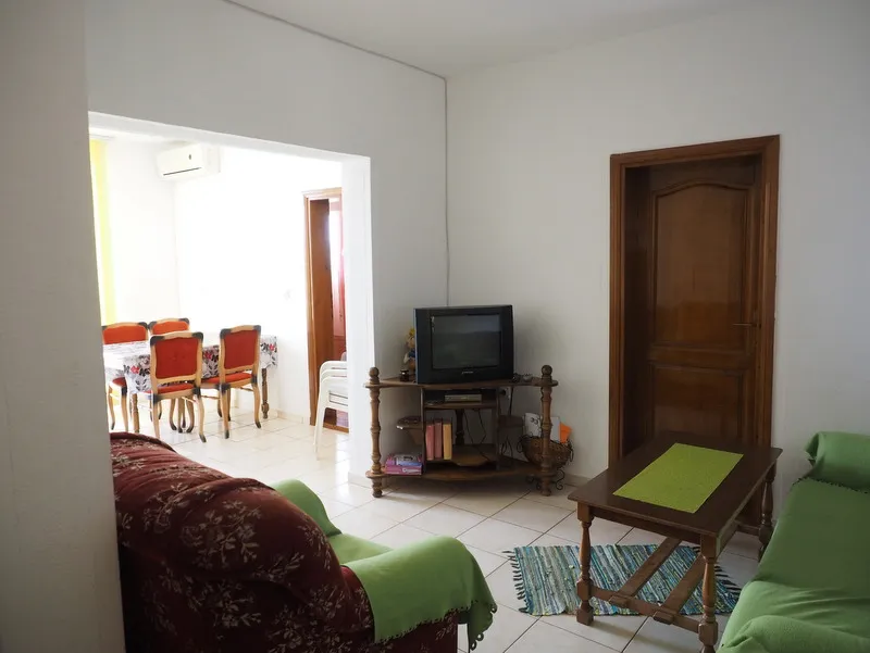 Living room with sofas, TV on a wooden stand, and coffee table; dining area visible through the archway.