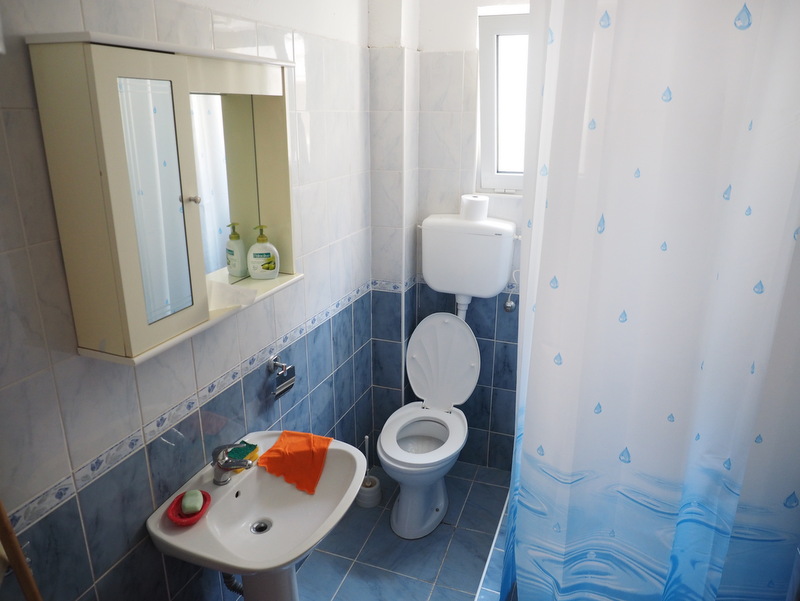 Bathroom in a house in Bar, Montenegro: light-colored tile, sink, toilet, and shower area with a curtain.