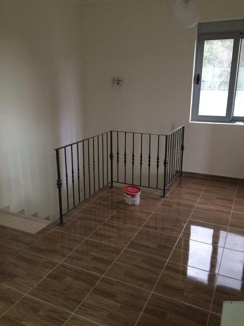Living room with staircase and wrought-iron railings in a house, Shushan, Montenegro. Light finishes and wood-look tile flooring.