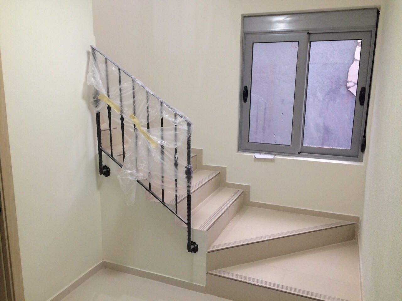 Staircase with wrought-iron railings and light tile in a new house in Shushan, Montenegro. Interior finish, view of the window.