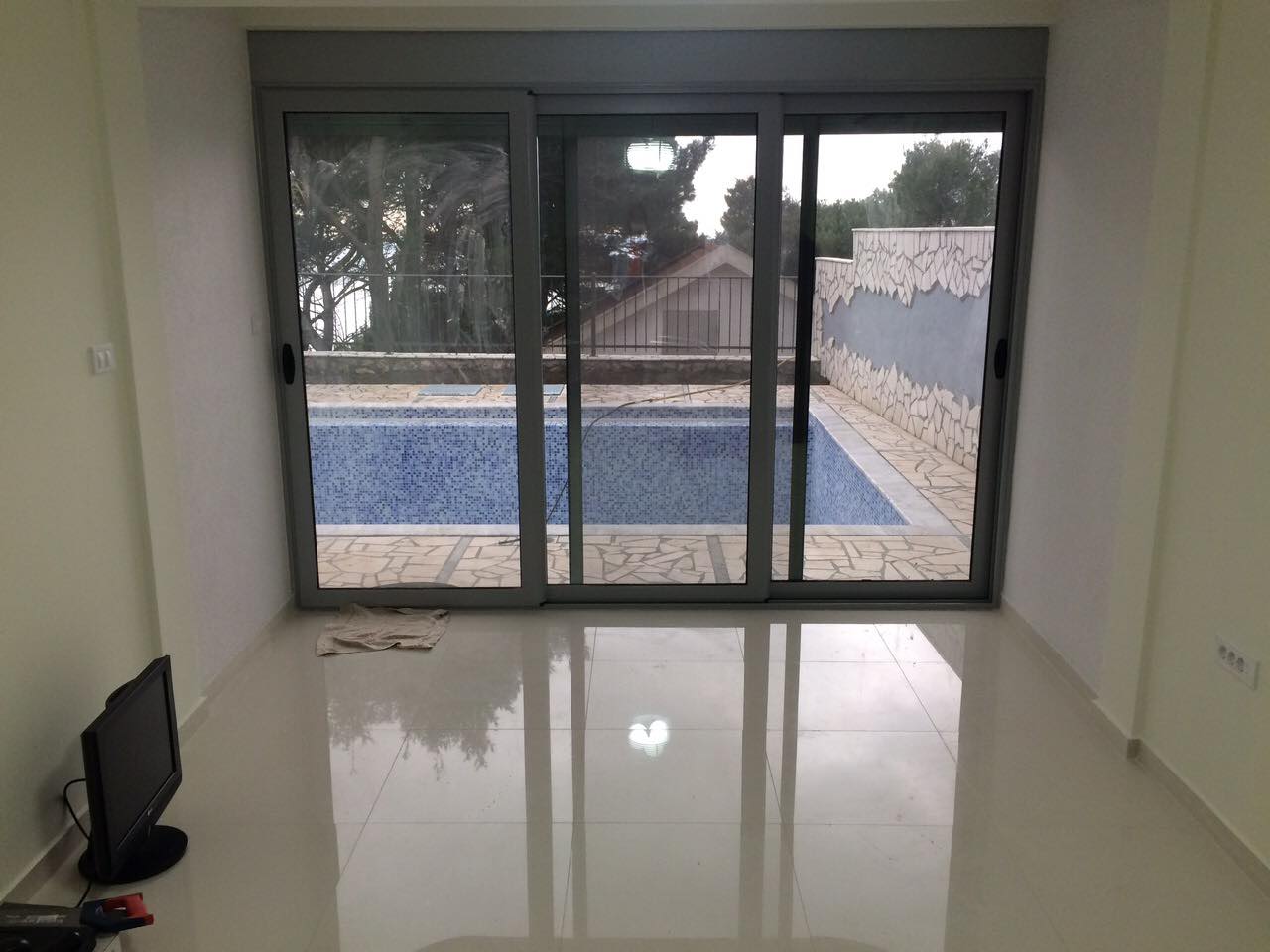 Living room with a panoramic window and access to the pool in a house, Shushan, Montenegro. Bright interior with a glossy floor.