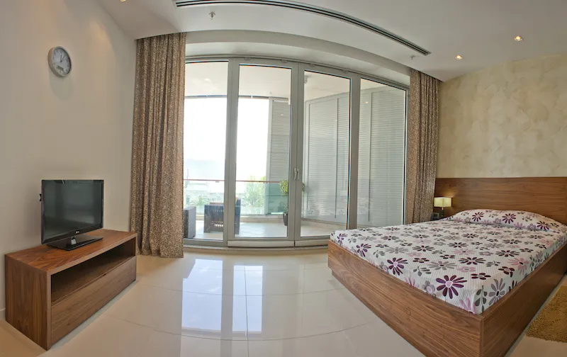 Bedroom featuring a wooden bed with floral bedding, a TV on a stand, and large glass doors leading to a balcony.