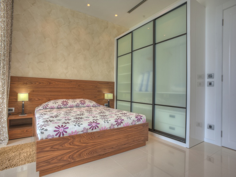 Modern bedroom in an apartment in Budva, Montenegro: a double bed with a wooden headboard and a built-in wardrobe.