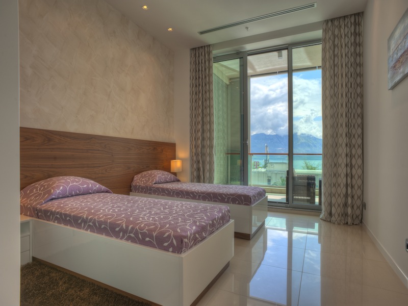 Bedroom in an apartment in Budva, Montenegro: two beds, a panoramic window with a sea and mountain view, modern finishes.