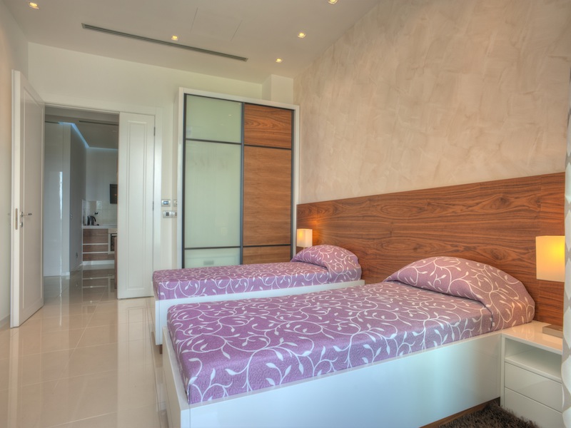 Modern bedroom with two beds in an apartment in Budva, Montenegro: built-in wardrobe, light finishes, and tile flooring.