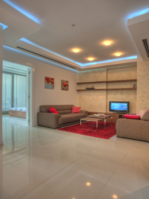 Modern living room in an apartment in Budva, Montenegro: beige furniture, red rug, ceiling lighting, and tile flooring.