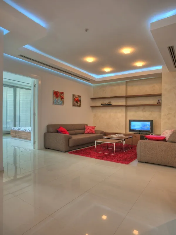 Living room with brown sofas, red rug, TV, and shelves on a textured wall under recessed lighting.