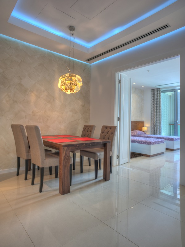 Modern living room with dining area in an apartment in Budva, Montenegro: wooden table, upholstered chairs, and LED lighting.
