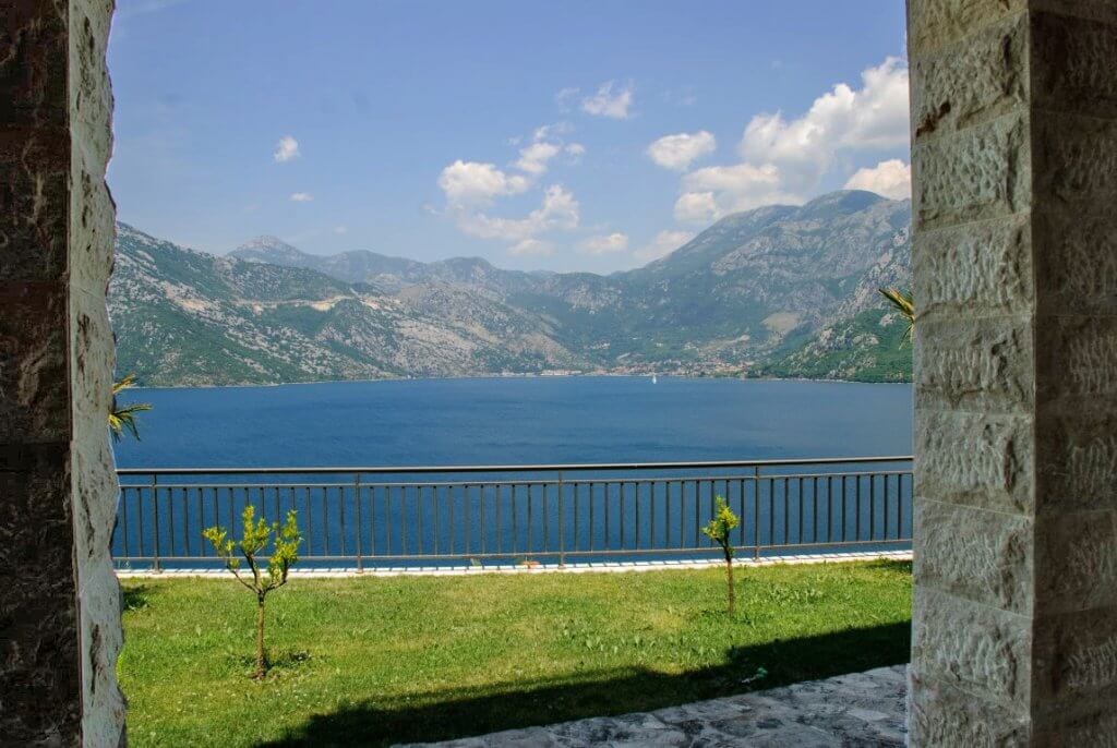 View of Kotor Bay and the mountains from the apartment terrace in Kostanjica, Montenegro: stone columns and a green lawn.