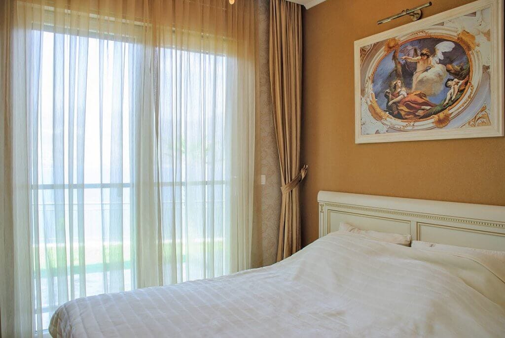 Cozy bedroom with a white bed and a painting in an apartment in Kotor, Montenegro, view of the terrace through a panoramic window.