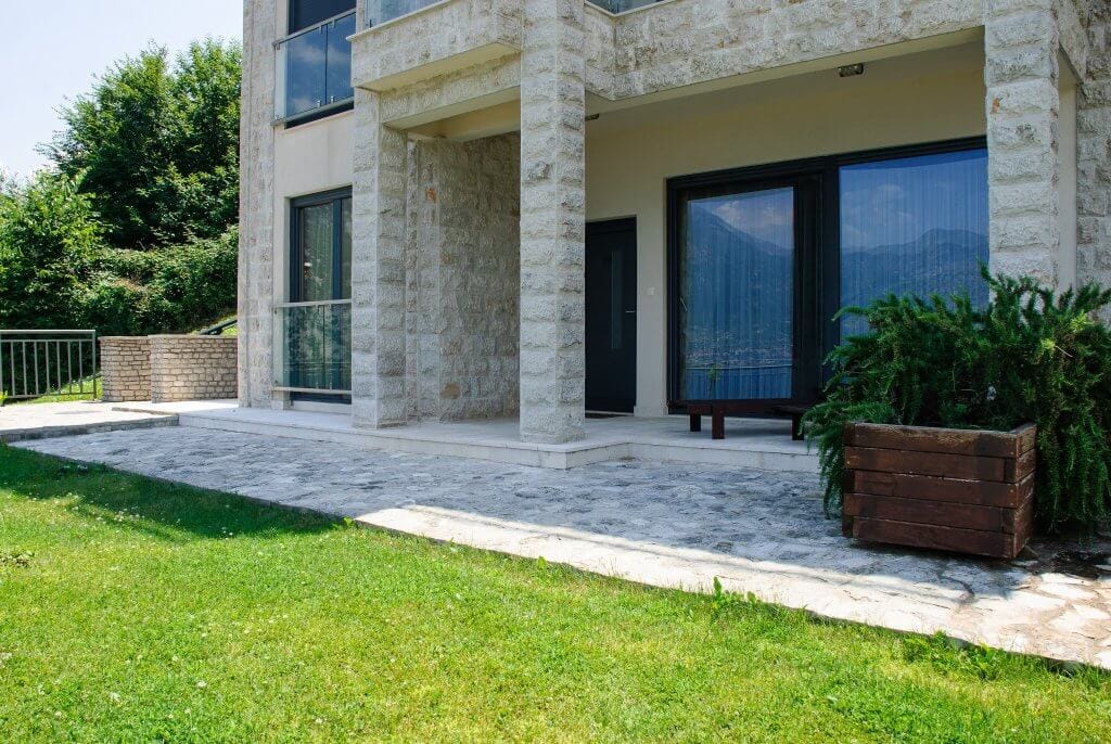 Apartment terrace in Kostanica, Montenegro: stone facade finish, panoramic windows, and views of the mountains and sea.