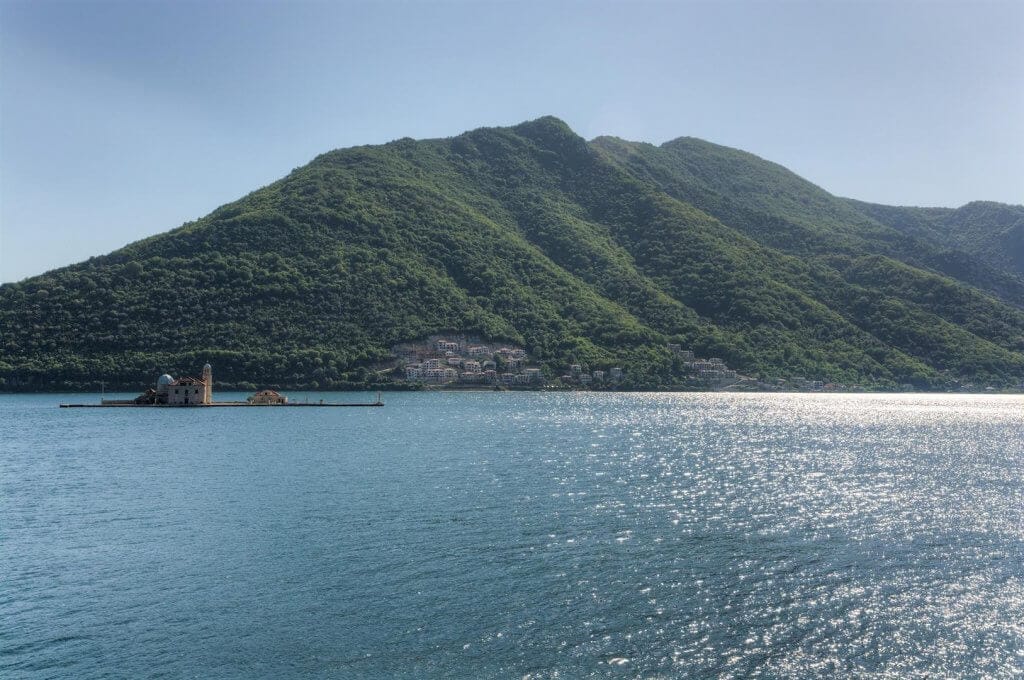 Panoramic view of the Bay of Kotor and the island of Our Lady of the Rocks in Kostanjica, Montenegro, with green mountains in the background.