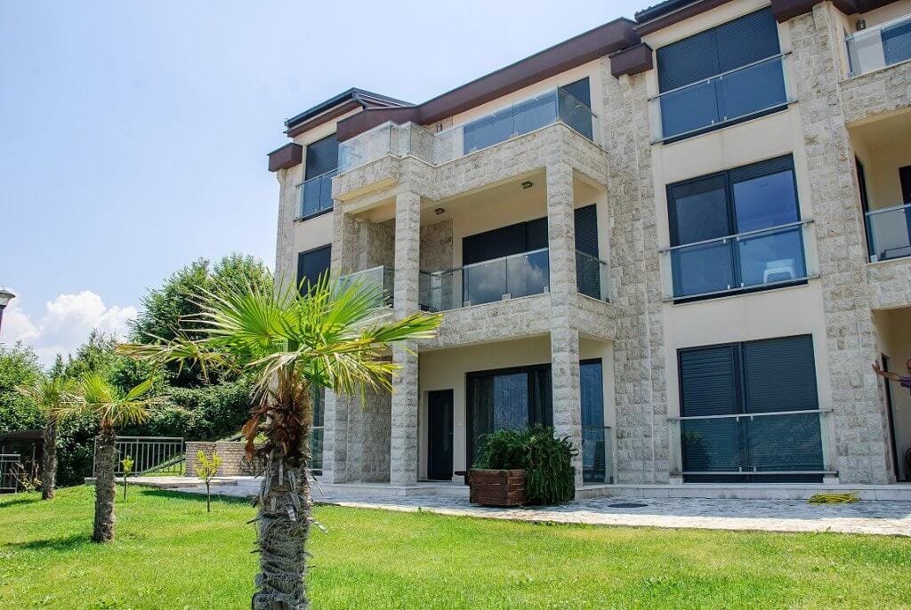 Modern residential complex with stone finishes and terraces in Kostanica, Montenegro, against a green garden backdrop.