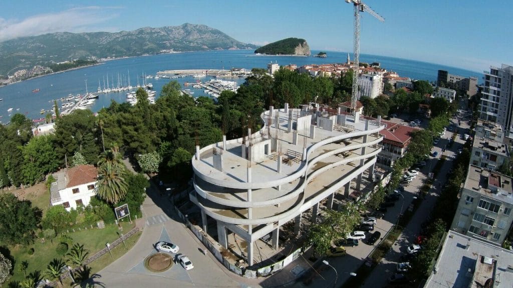 Residential complex under construction in Budva, Montenegro: aerial view of a concrete building by the sea and the yacht marina.