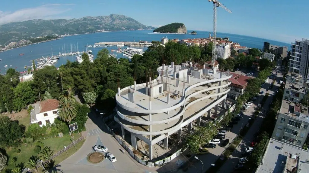 Aerial view of an unfinished building under construction near a harbor with a crane.