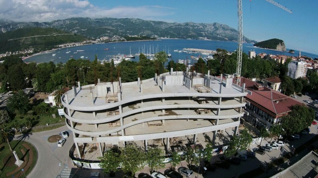 Residential complex under construction in Budva, Montenegro: aerial view of the building’s concrete frame by the sea and yacht marina.