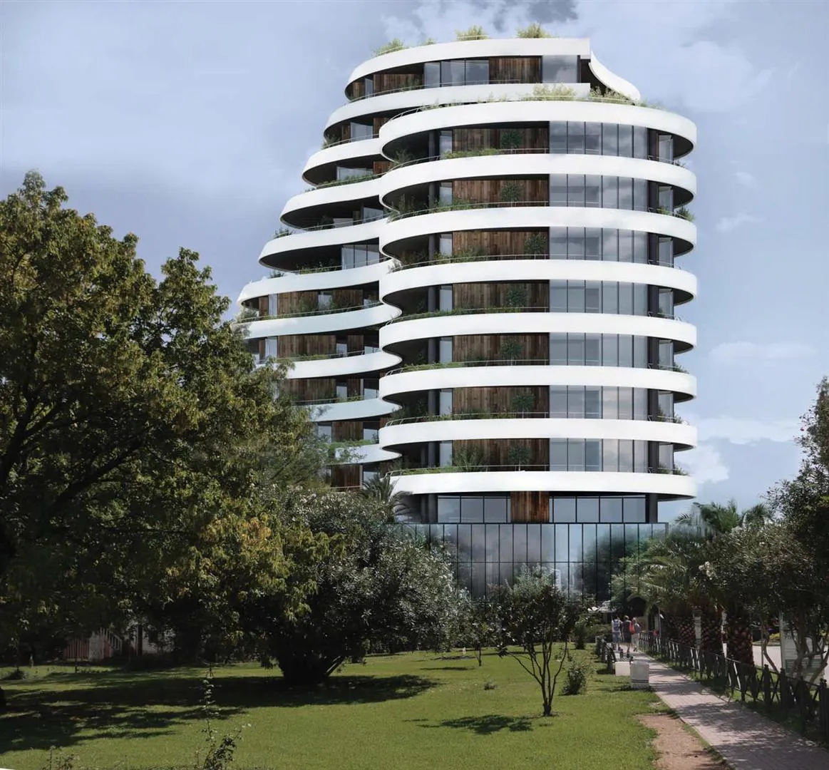 Modern high-rise building with curved white balconies and wood paneling surrounded by green trees and lawn.