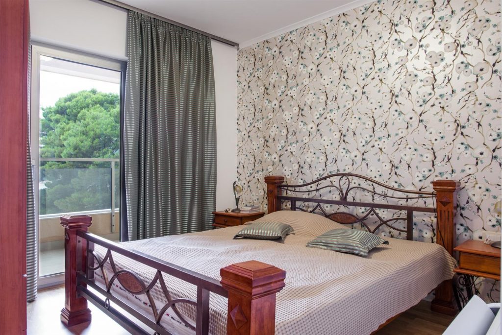 Bedroom with a double bed, floral wallpaper, and access to the balcony in an apartment, Becici, Montenegro.