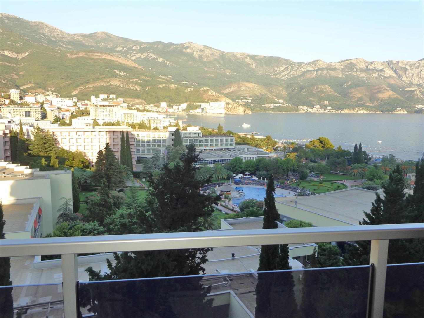View from the balcony of the sea, mountains, and the Becici resort in Montenegro, a panoramic view of the coastline with hotels and a pool.