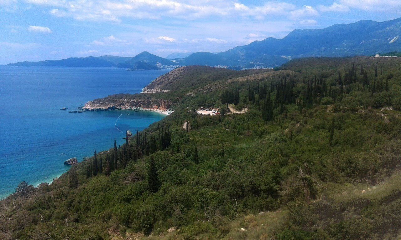 Panoramic view of the Adriatic Sea and mountains from a villa in Reževići, Montenegro: a green hillside, cypress trees, and a wild beach.