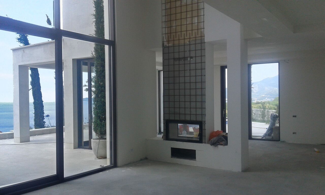 Living room in a villa in Reževići, Montenegro: panoramic windows, sea view, fireplace under finishing, and terrace.