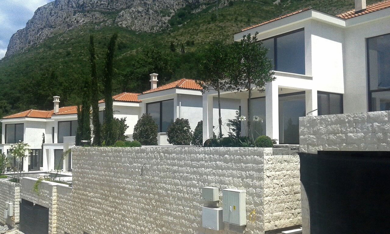 Modern villas with panoramic windows and stone finishes in Reževići, Montenegro, against a mountain backdrop.