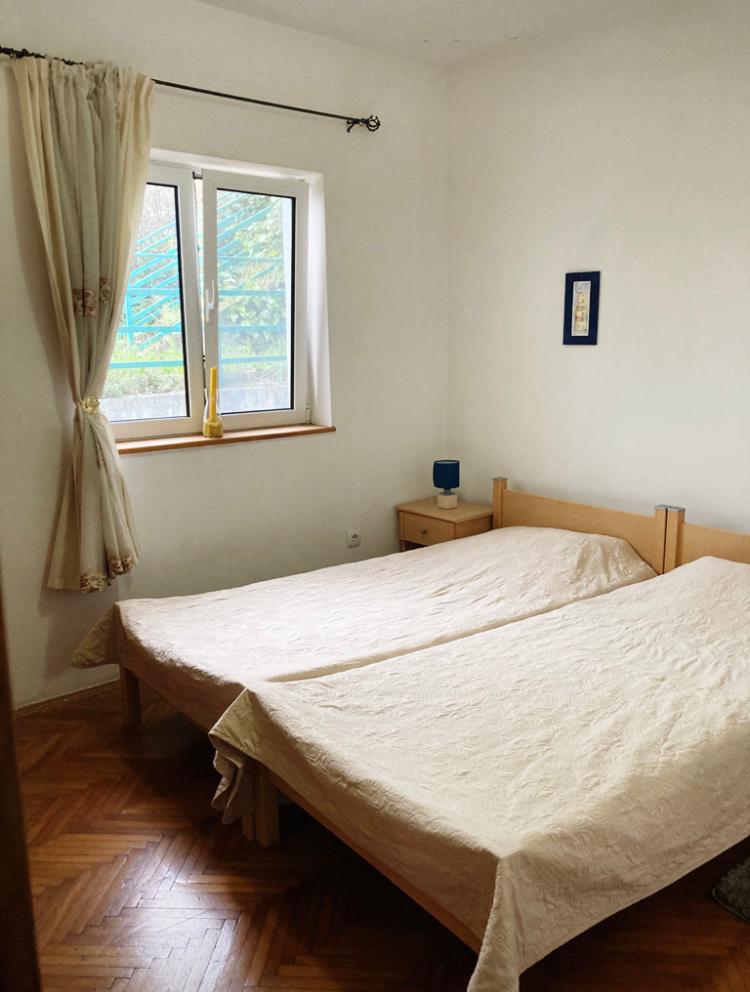 Bedroom in a hotel in Budva, Montenegro: two single beds, wooden floor, light walls, and a window overlooking the street.